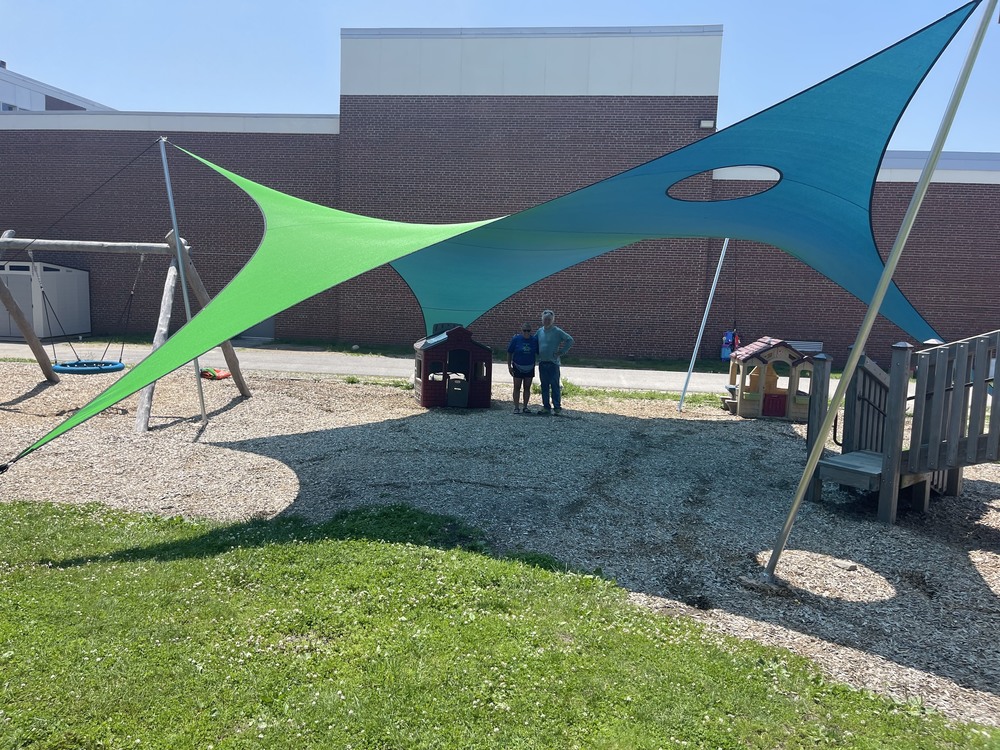 A green and blue canopy is above two employees on the PC playground